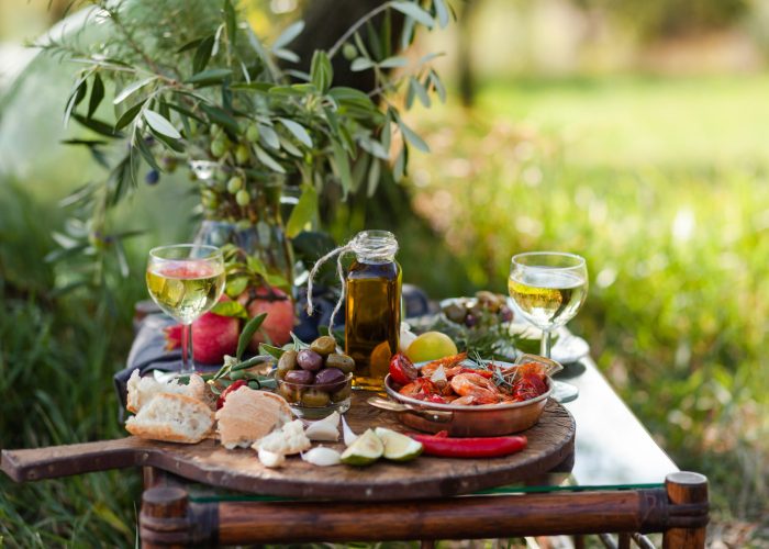 Romantic italian lunch outside for a couple: copper pan with delicious and spicy fried shrimps with herbs and garlic, wine, bread, olives. Bottle of olive oil. Luxury lifestyle, gourmet food
